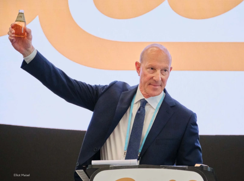 Elliot Maisel speaking at a podium, holding up a beverage bottle in front of a Gulf Distributing backdrop