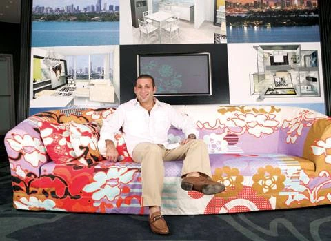 Keith Menin seated on a colorful couch in a design-filled interior, smiling at the camera